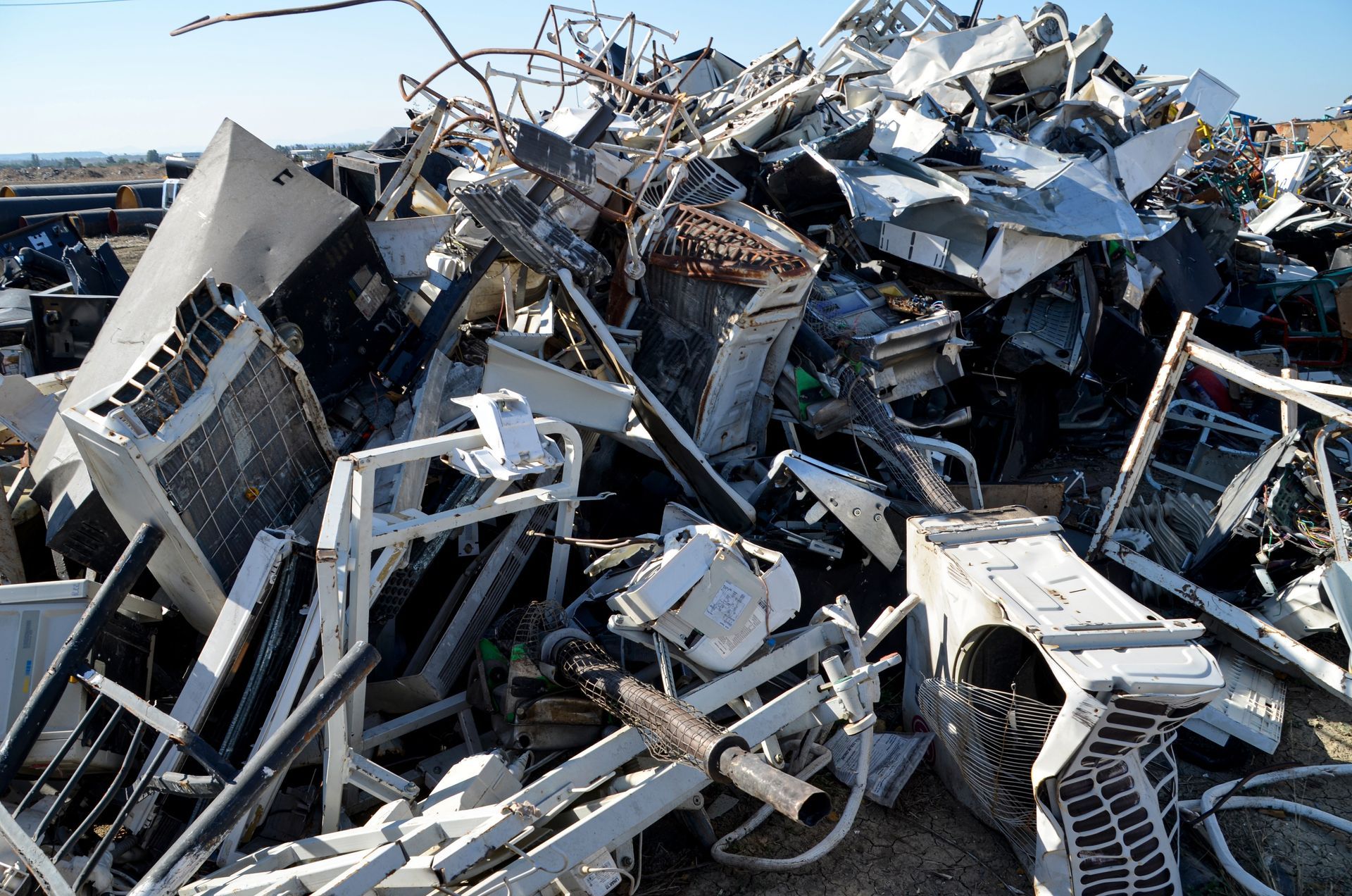 Pile of twisted metal and scrap debris in an outdoor junkyard under a blue sky