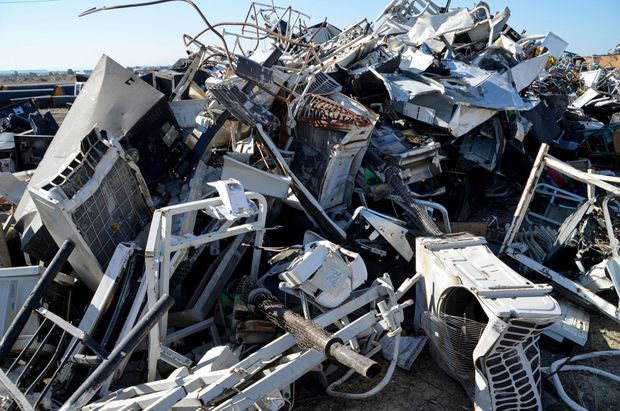 Pile of twisted scrap metal and broken machinery in a junkyard under a blue sky