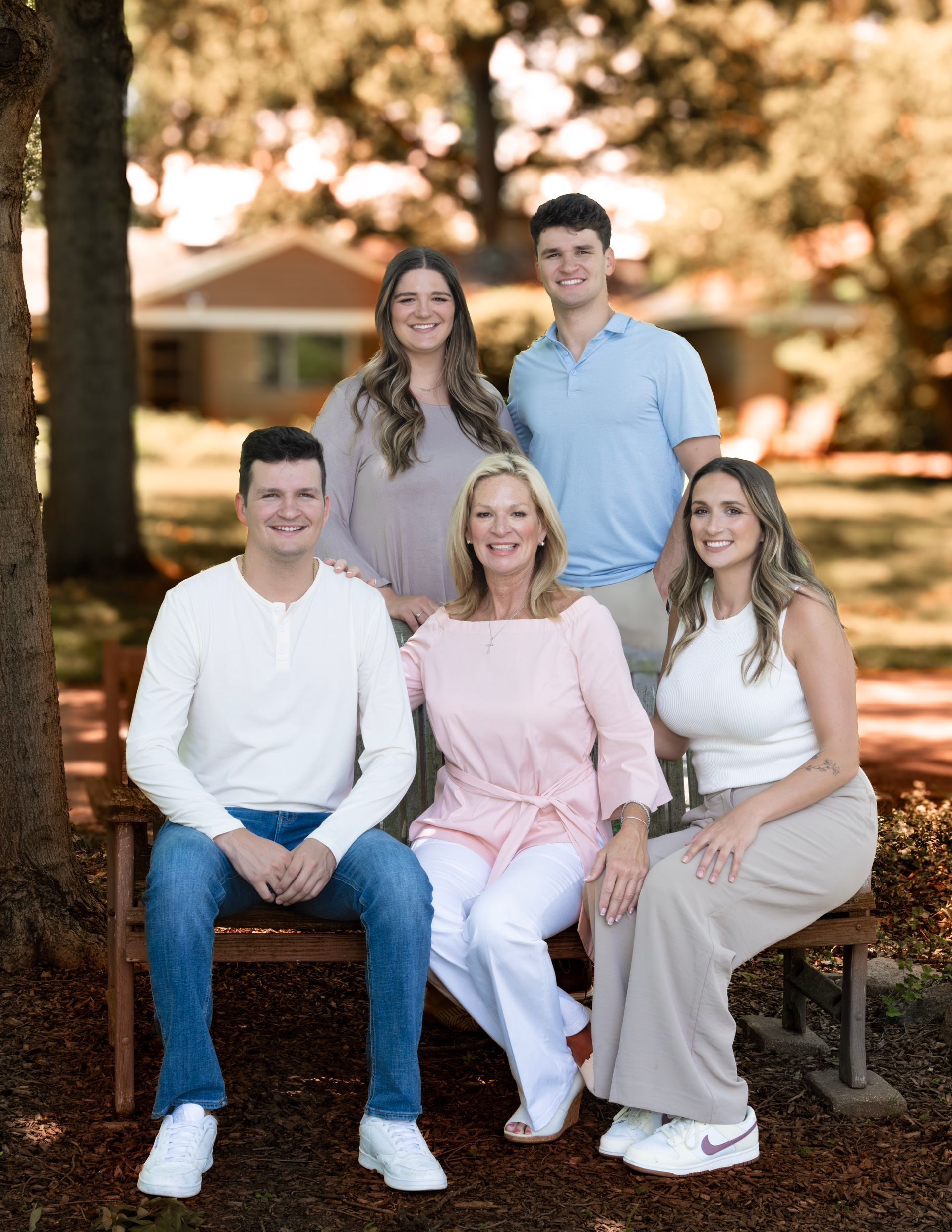 Family portrait in front of a house: six people, all smiling, seated on a bench, wearing light-colored clothes.
