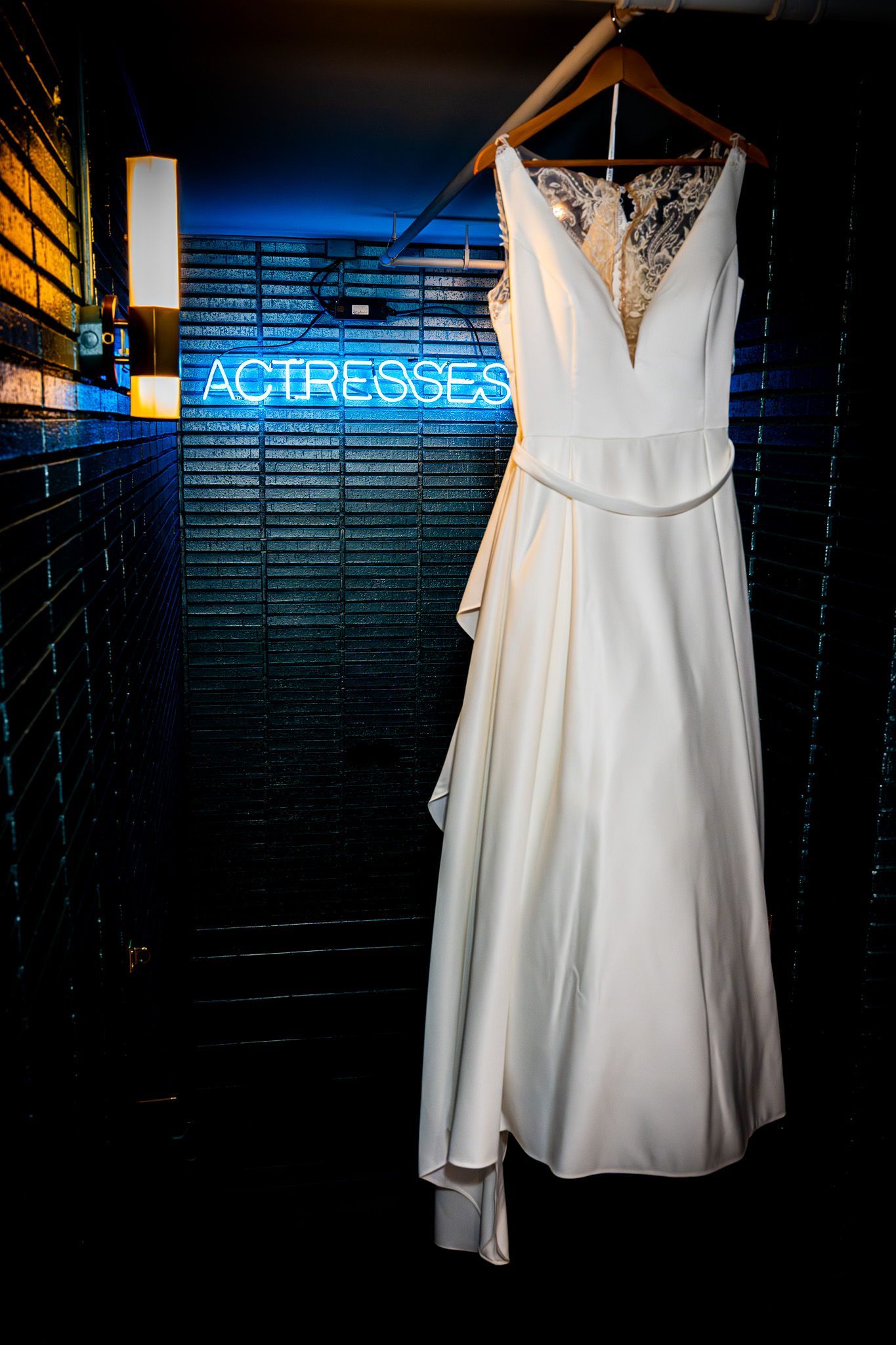 Wedding dress hanging against a neon sign in a dark room.