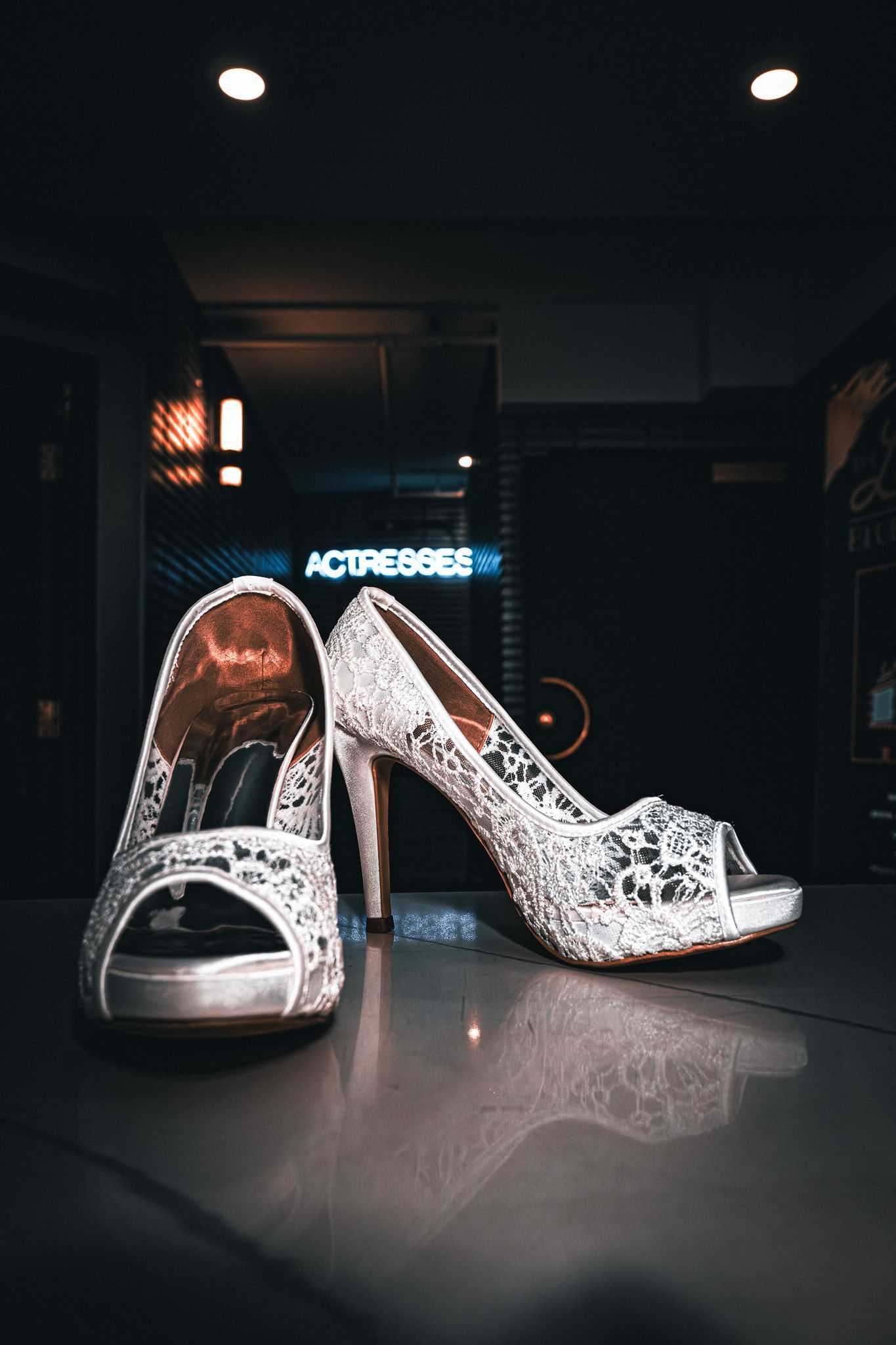 Silver high heels on a reflective surface, with an illuminated background.