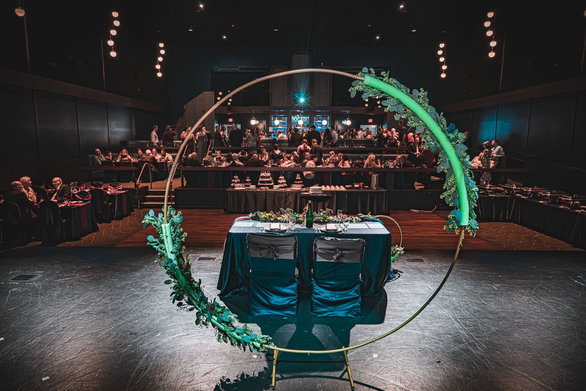 Ceremony stage with a decorated gold circle and table, audience seated in a dark theater.