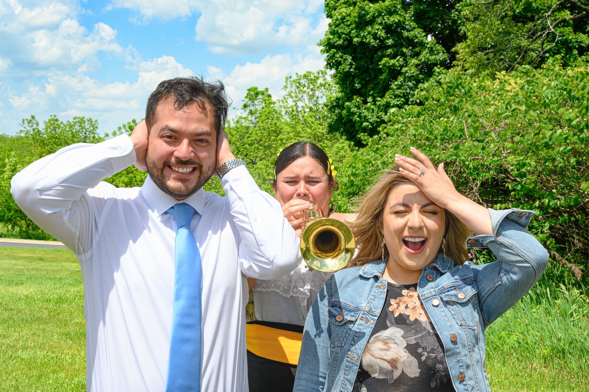 Three people reacting to a trumpet player outdoors. One covers ears, one plays, and one covers their head.