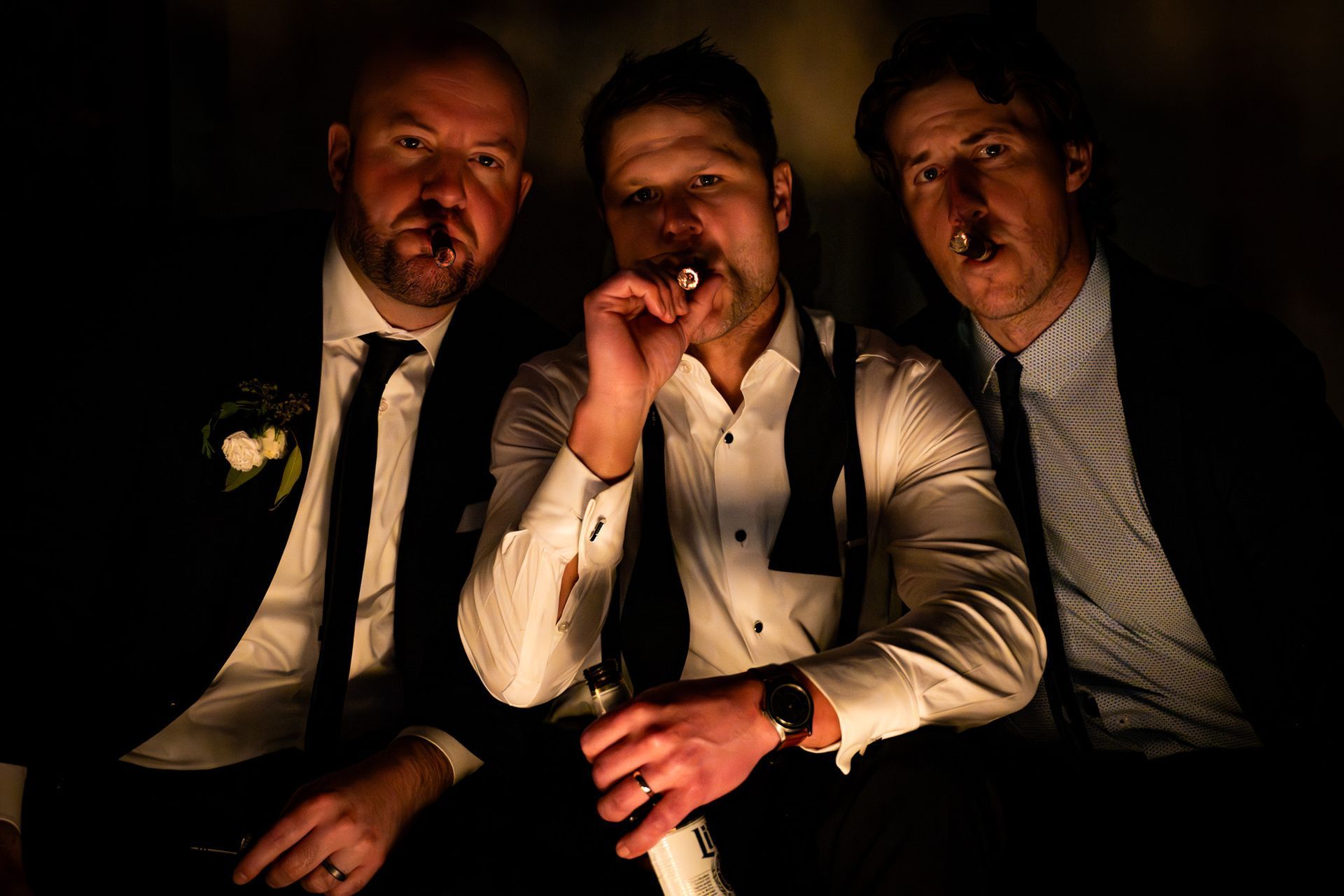 Three men in formal wear smoking cigars. Dimly lit, close-up shot.