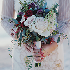 Bride holding a bouquet of burgundy and cream-colored flowers with greenery.