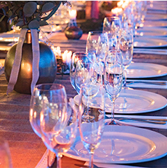 Long dining table set with white plates, crystal glasses, and gold decor.
