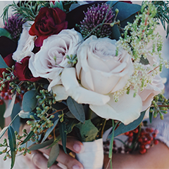 Close-up of a bridal bouquet with white and burgundy roses, greenery, and berries.