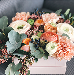 Floral arrangement in a light pink box, featuring peach, white, and green blooms with eucalyptus leaves and berries.