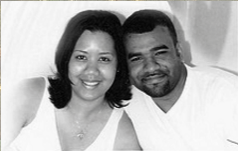 Smiling couple seated close together on a couch, wearing white tops.
