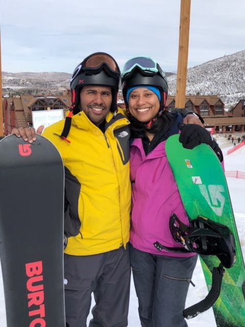 Two snowboarders in helmets holding snowboards, smiling on a mountain slope.