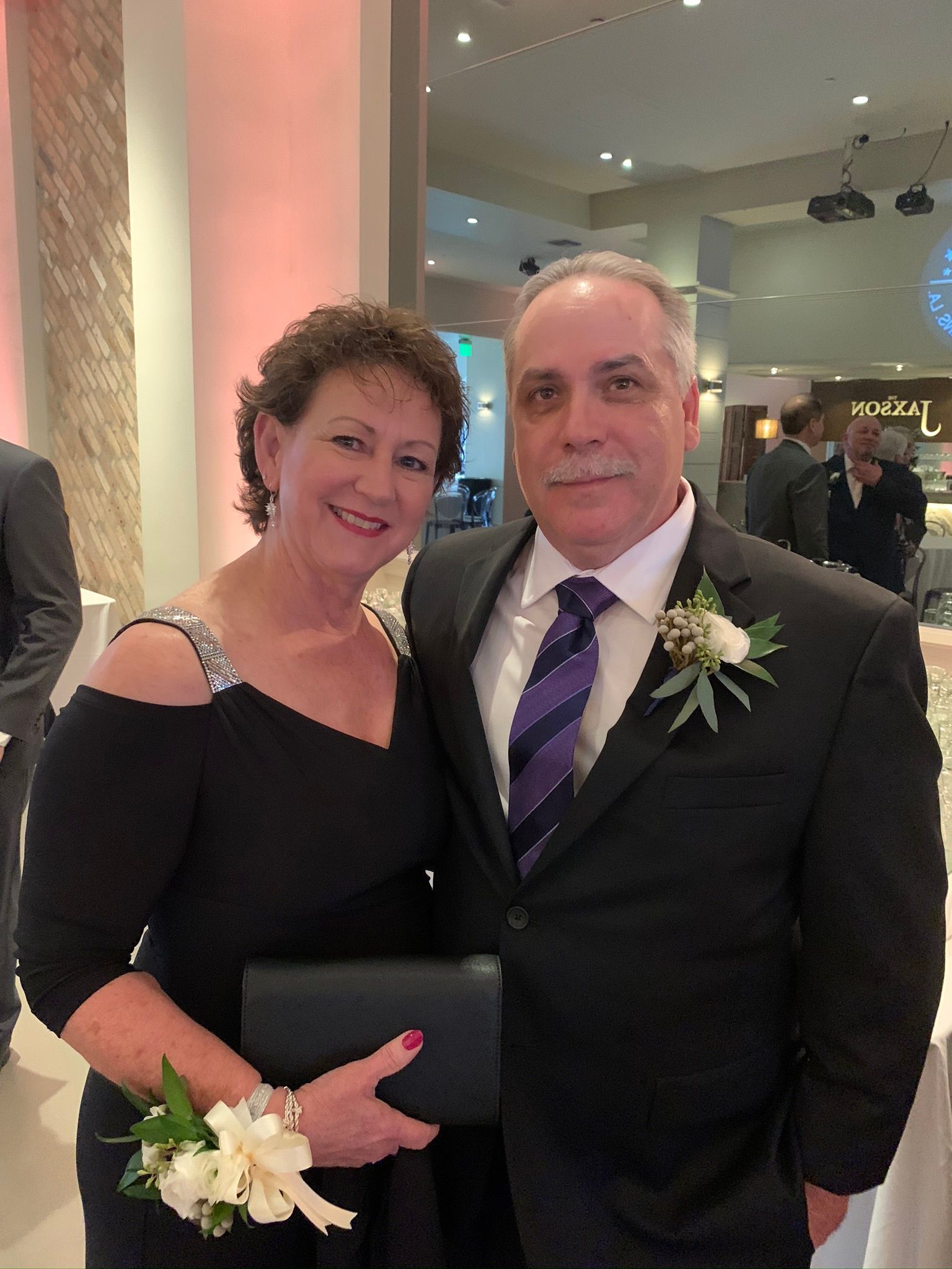 Couple in formal attire posing indoors, smiling beside a wedding arch.