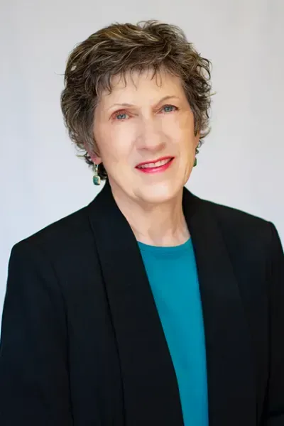 Studio portrait of a smiling woman in a black blazer and teal top against a light background