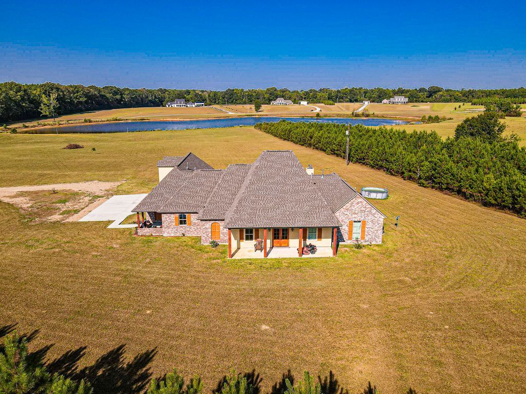 Aerial view of a thatched-roof house in a grassy field near water and trees.