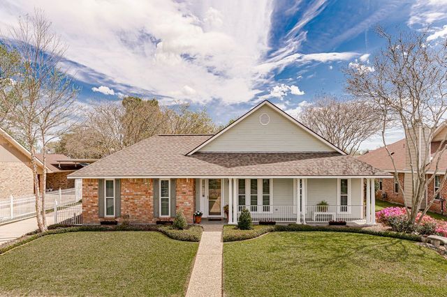 Single-story brick house with a front porch, walkway, and manicured lawn under a partly cloudy sky