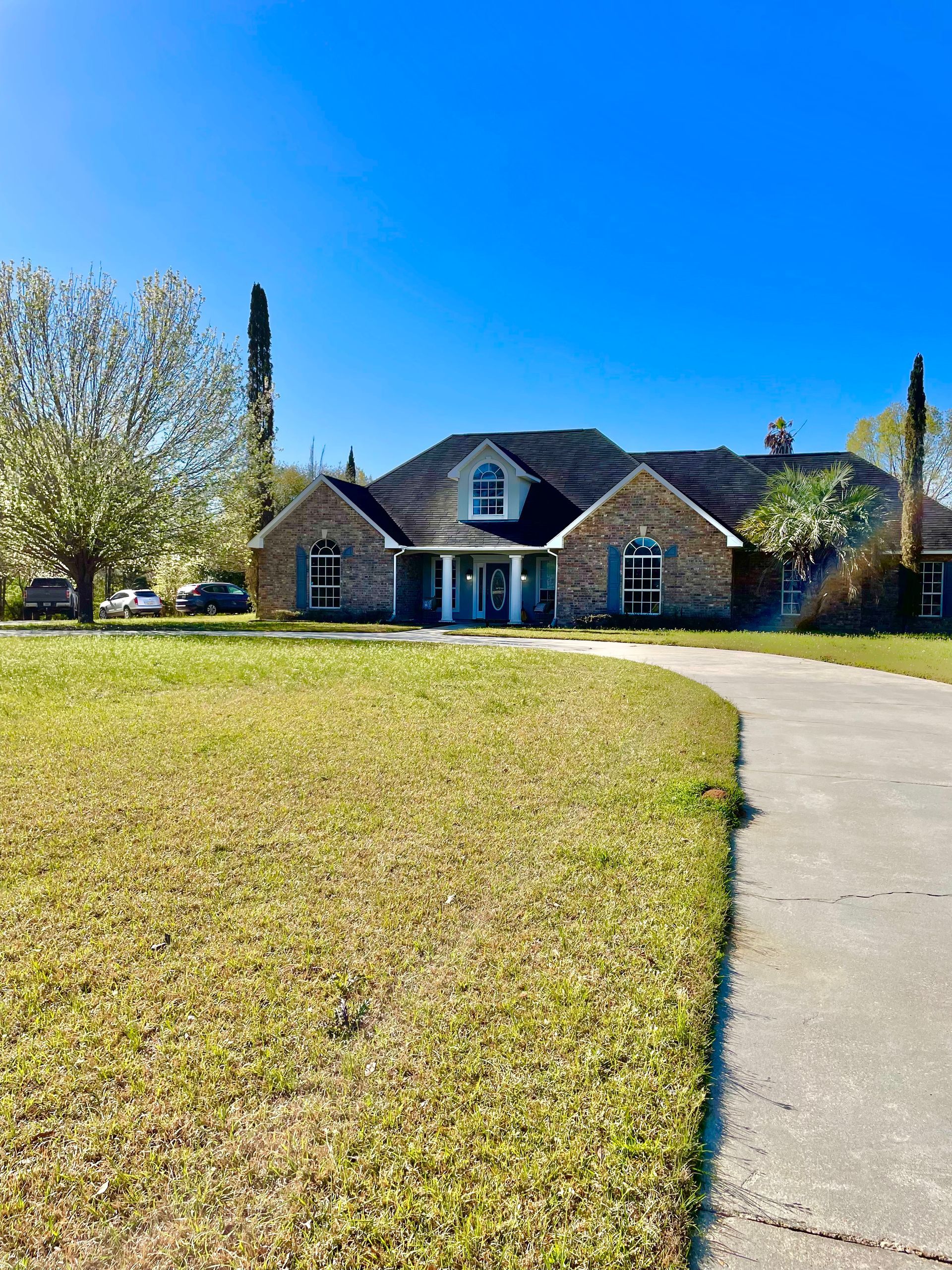 Brick house with a curved driveway and large grassy lawn under a clear blue sky