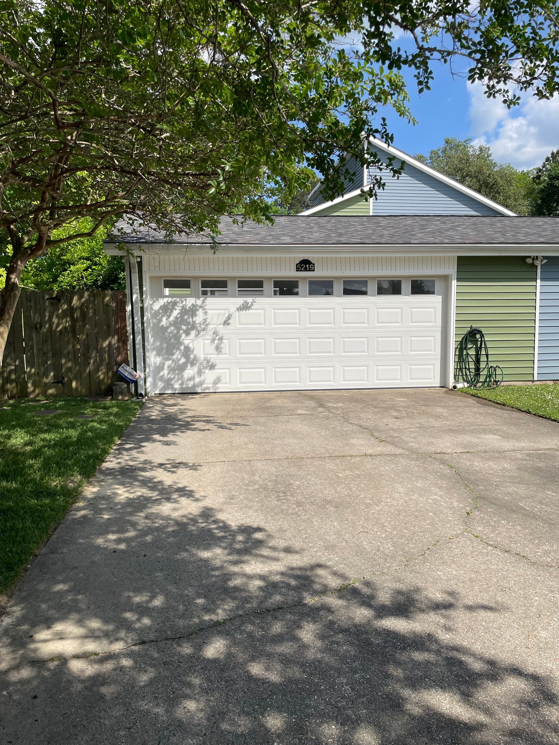 Driveway leading to a white two-car garage with green siding and tree shade overhead