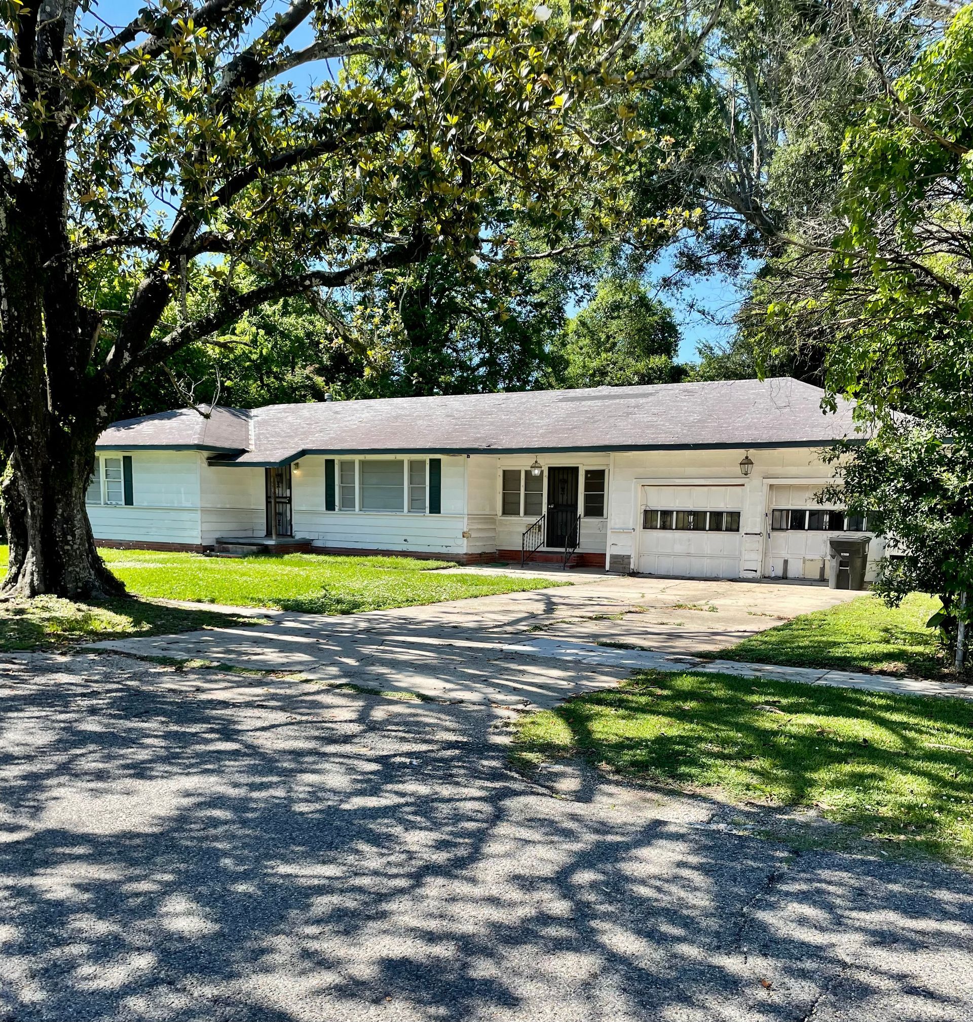 Single-story white house with attached garage and large trees lining the front yard