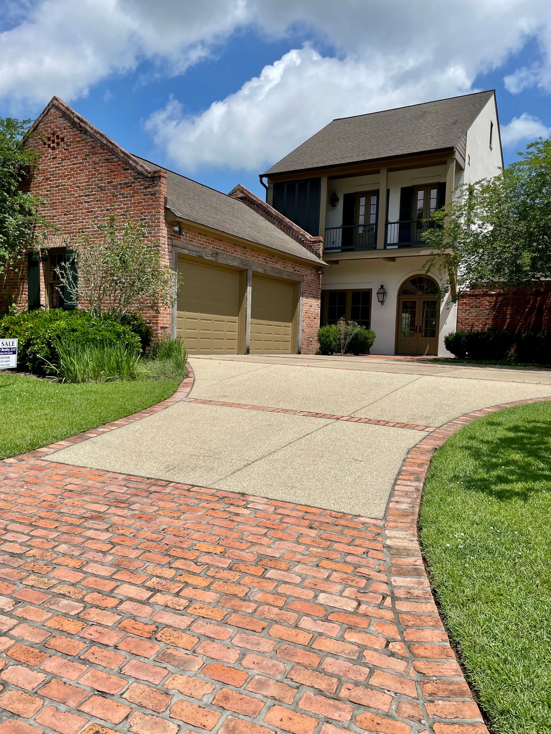 Brick driveway leading to a two-story house with a balcony and landscaped front yard
