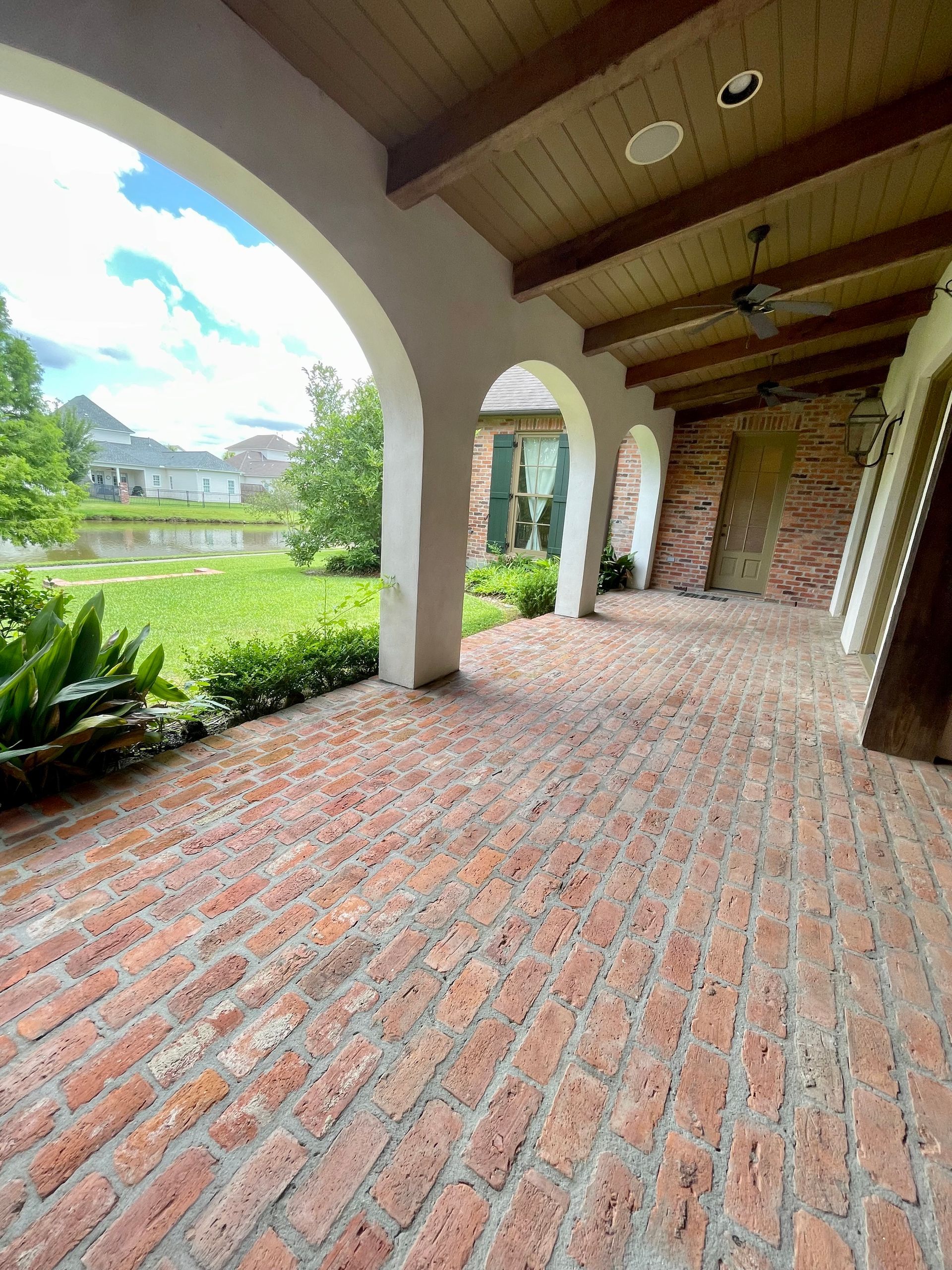 Covered brick patio with arched columns, wooden ceiling, and view of a green garden and distant hills.