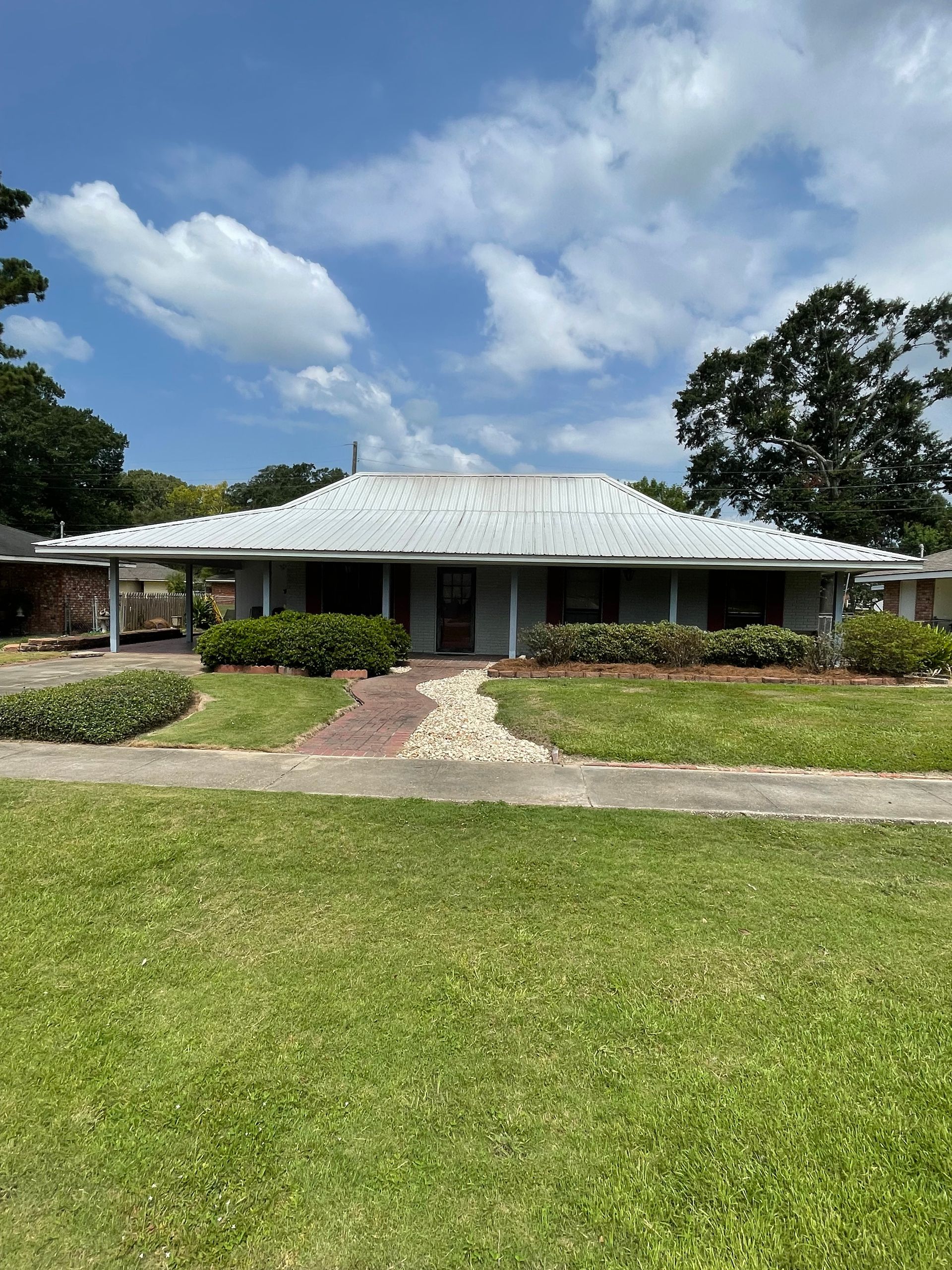 Single-story house with a wide porch, stone path, and green lawn under a partly cloudy sky