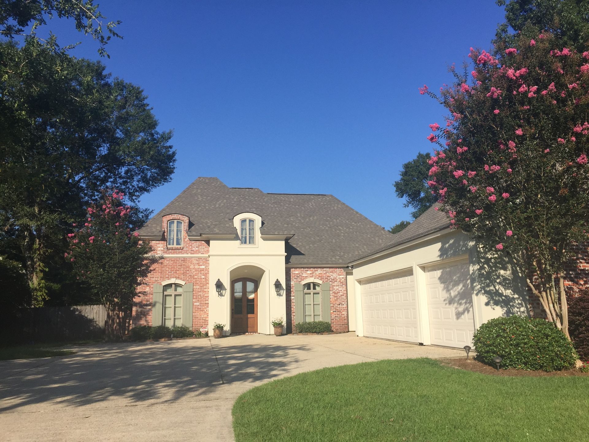 Suburban house with brick and stucco exterior, two-car garage, and flowering trees under a blue sky