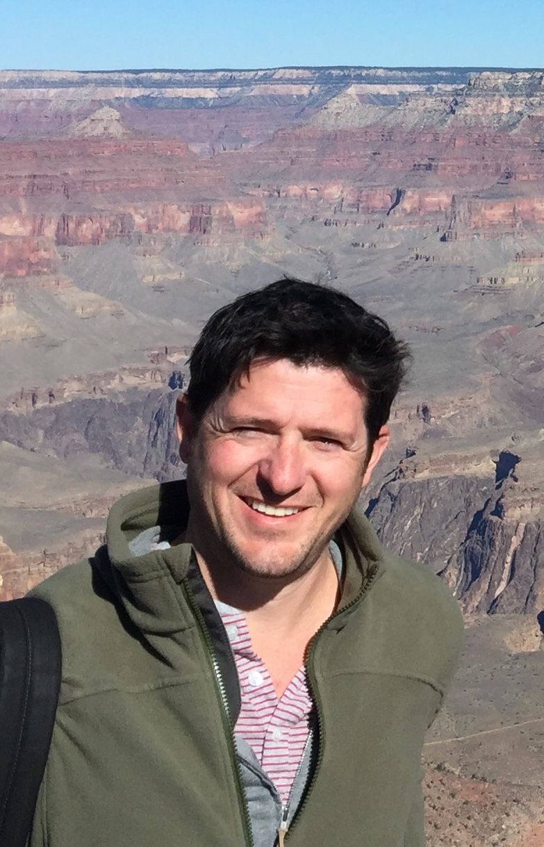 Smiling person in a green jacket with a canyon landscape in the background