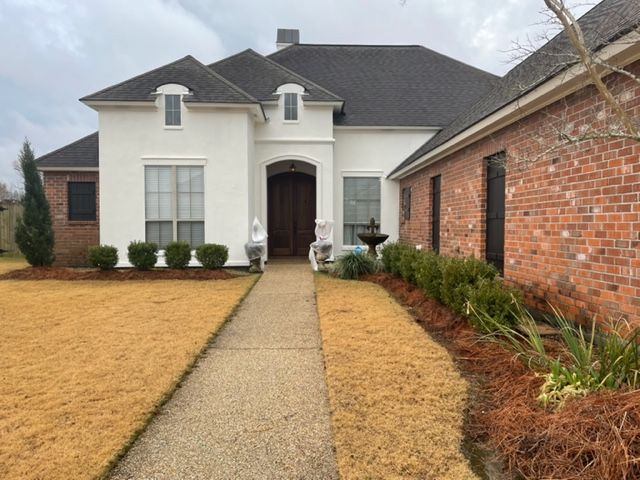 Front view of a white house with a brick side wall and a concrete walkway leading to the front door.