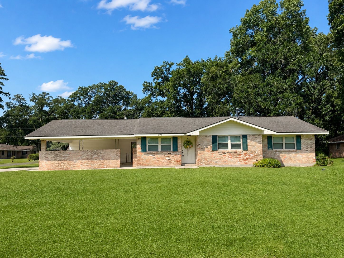 Single-story brick house with a wide lawn and trees in the background