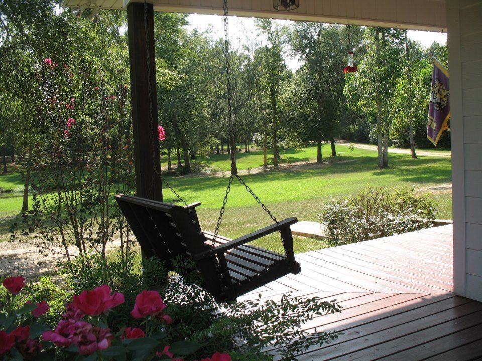 Covered porch with a hanging black swing overlooking a green yard and trees