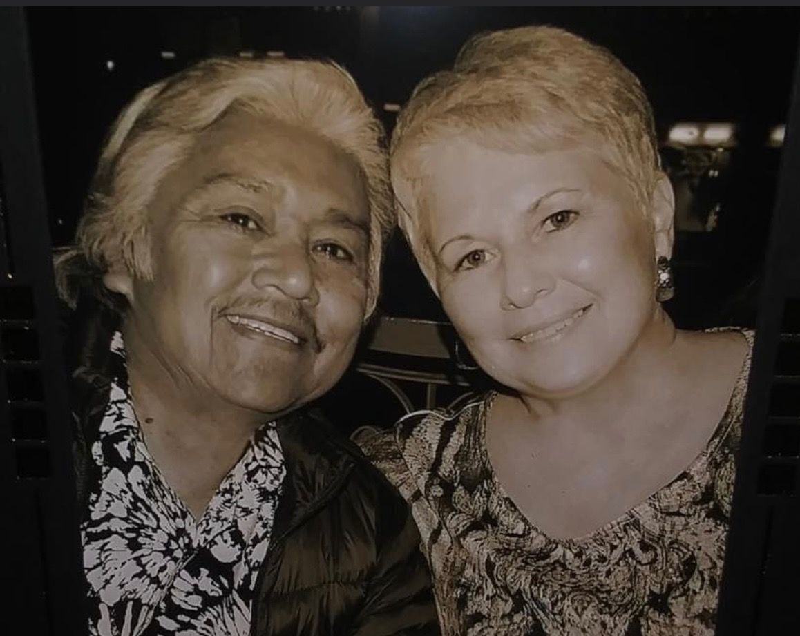 Two smiling women pose closely together in a dimly lit setting.