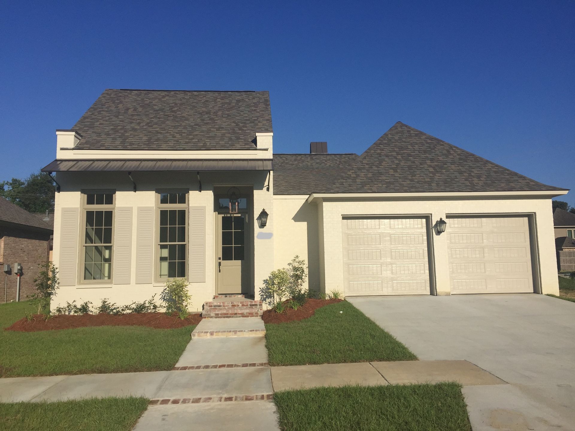 Suburban beige house with two-car garage, manicured lawn, and clear blue sky