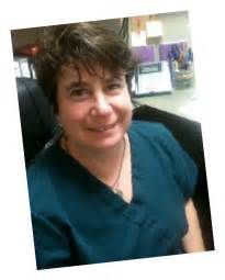 Smiling person in a teal top seated indoors at a desk, with a blurred office background