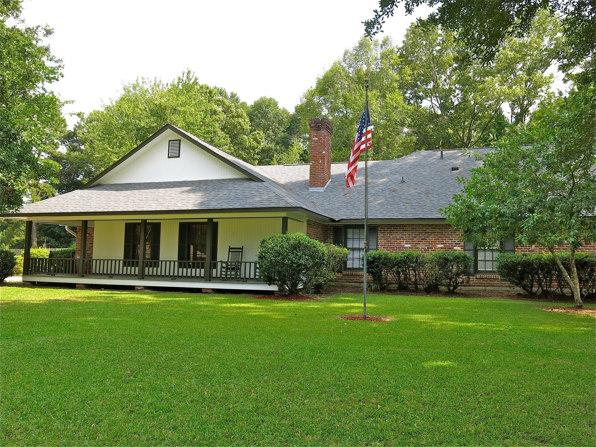 Single-story house with a covered porch, green lawn, and an American flag in front