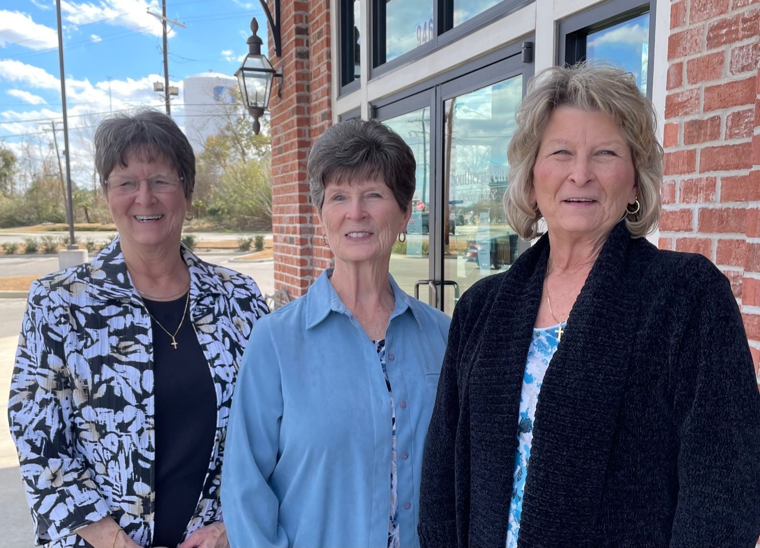 Three people standing outside a brick building in daylight, smiling at the camera.