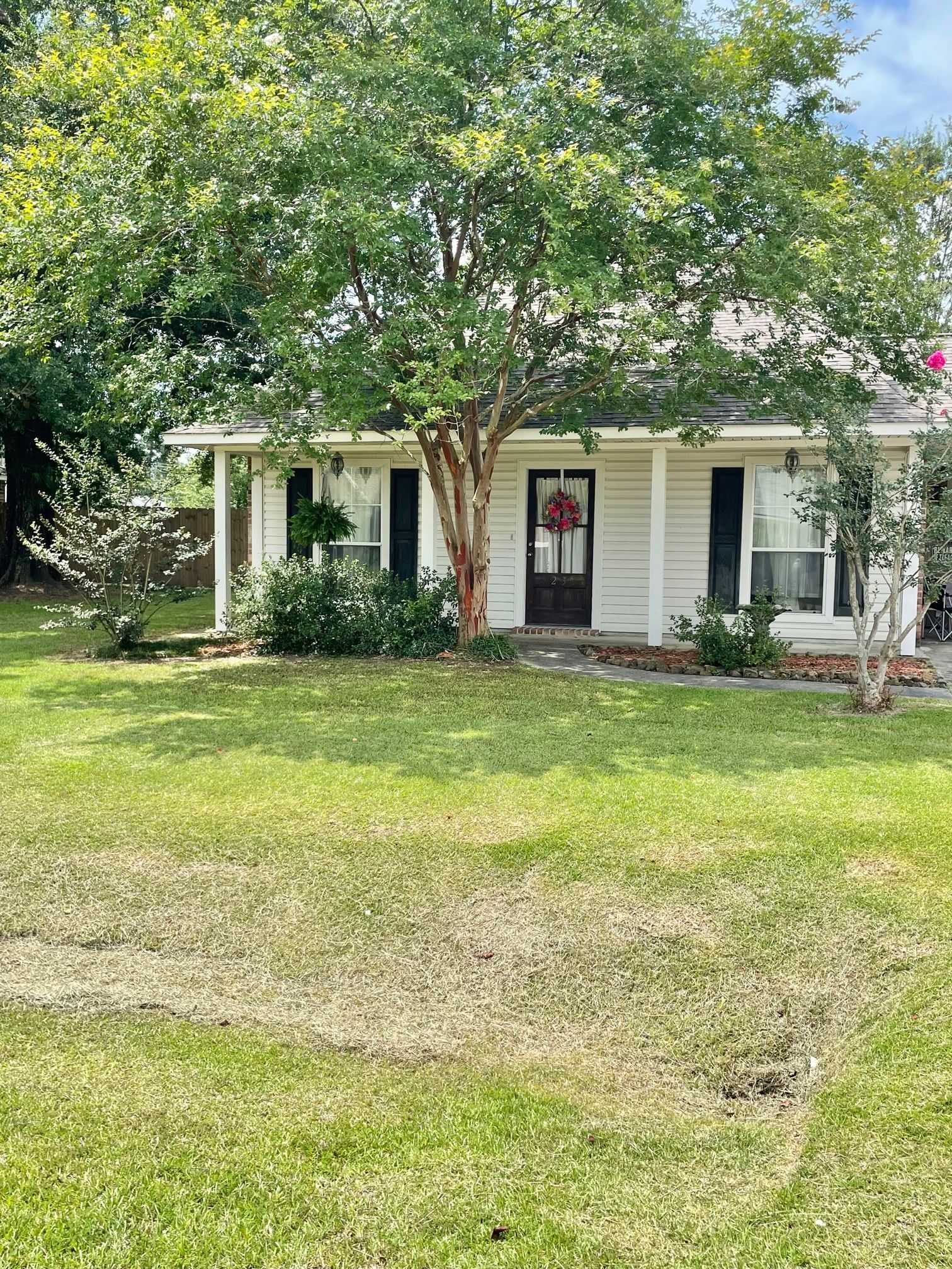 Small white house with a front porch, surrounded by trees and a grassy yard.