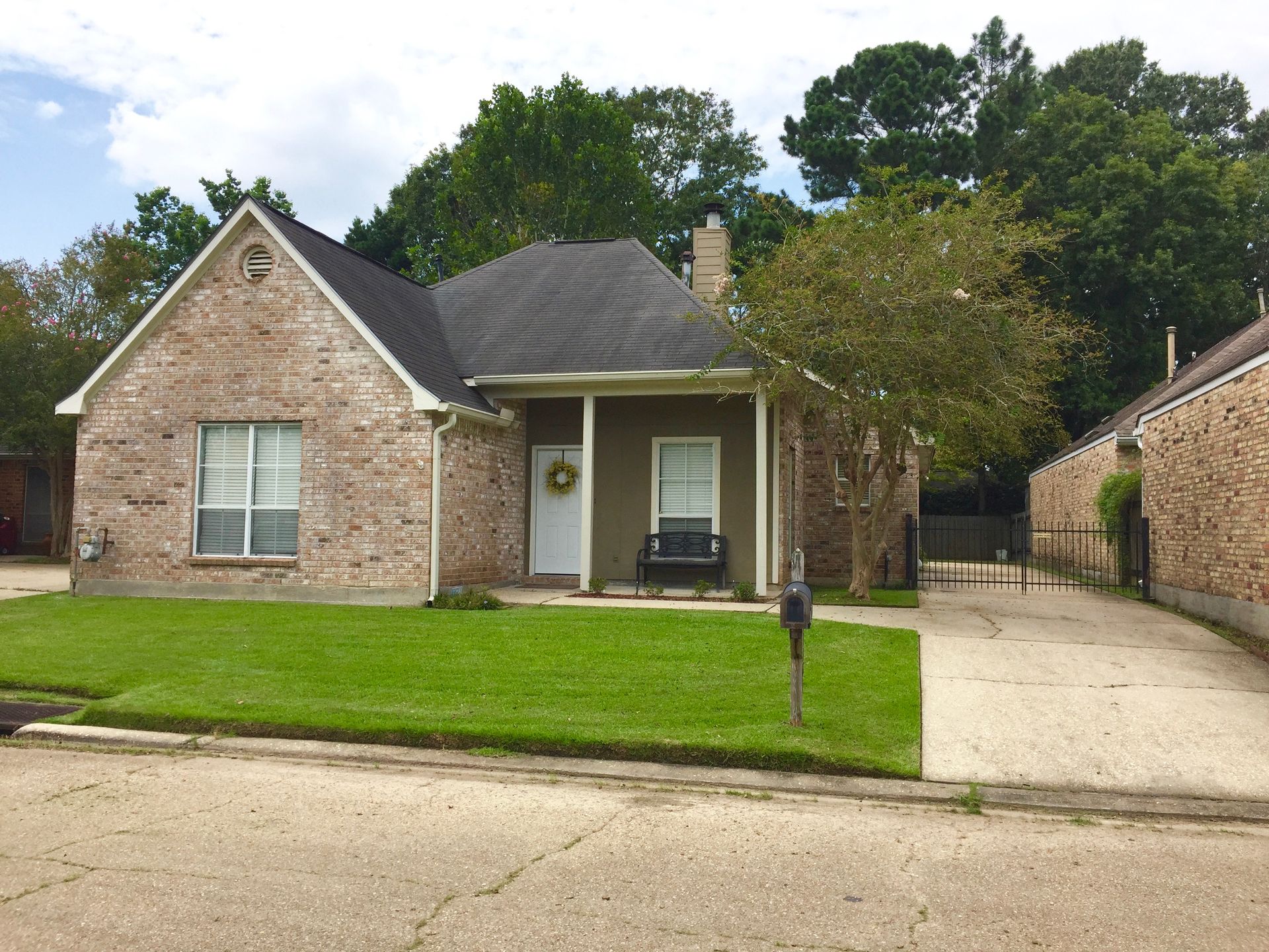 Brick single-story house with a green lawn, front porch, and driveway under cloudy skies