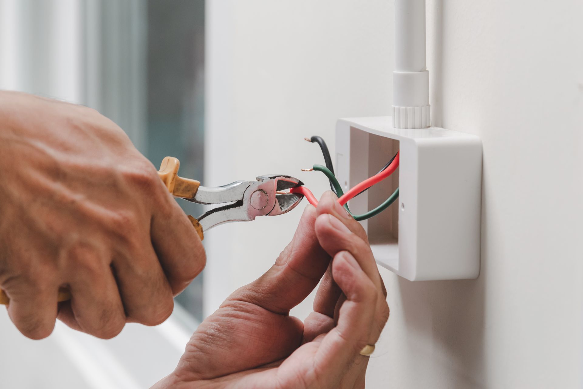A person is fixing a light switch with a pair of pliers.
