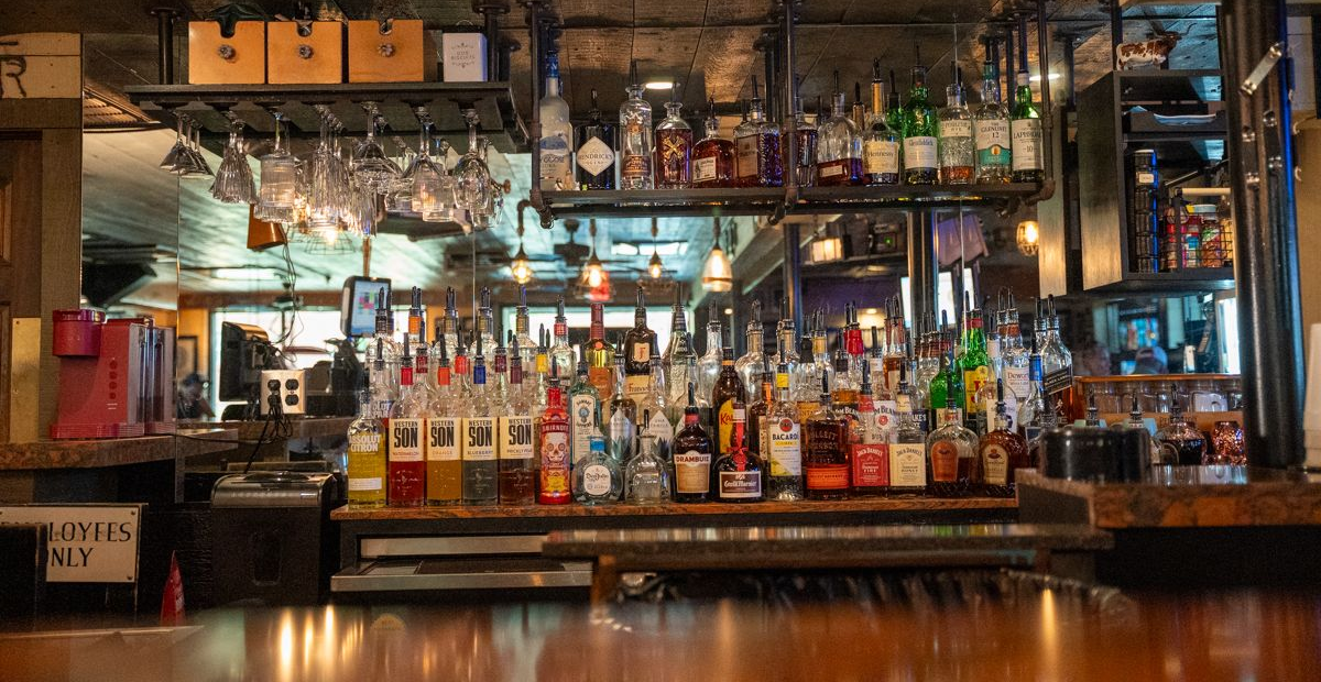 Bar with a variety of liquor bottles displayed on shelves. Wooden countertop.