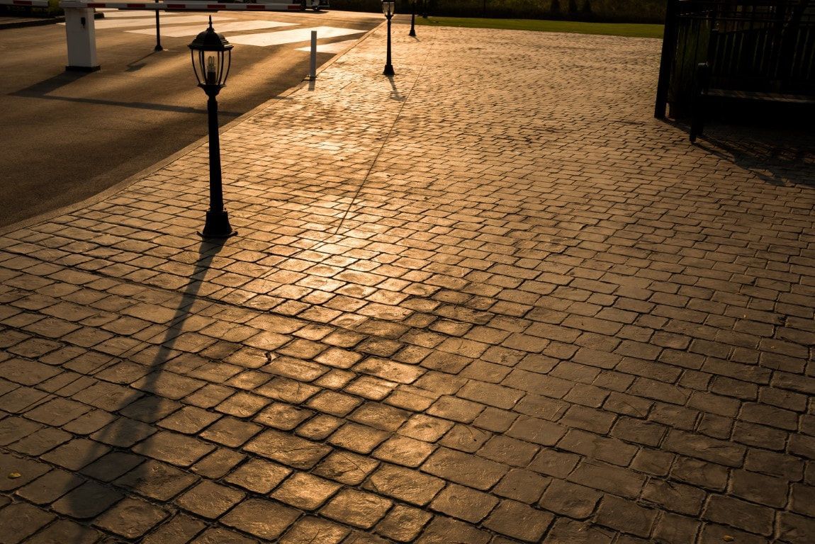 Cobblestone walkway at night lit by warm streetlights, with lamp posts and long shadows