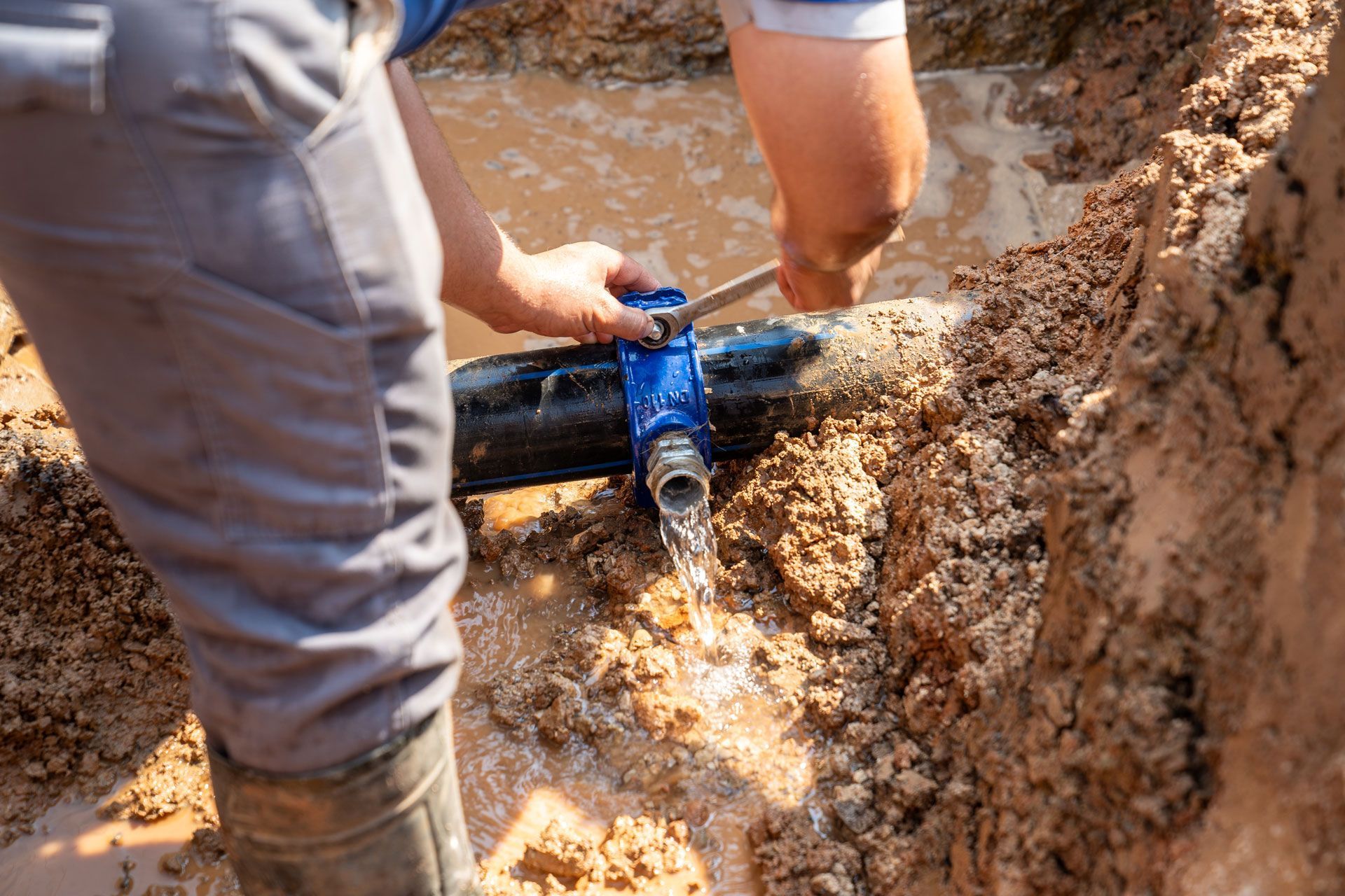 Worker installing a blue pipe connection in a muddy trench