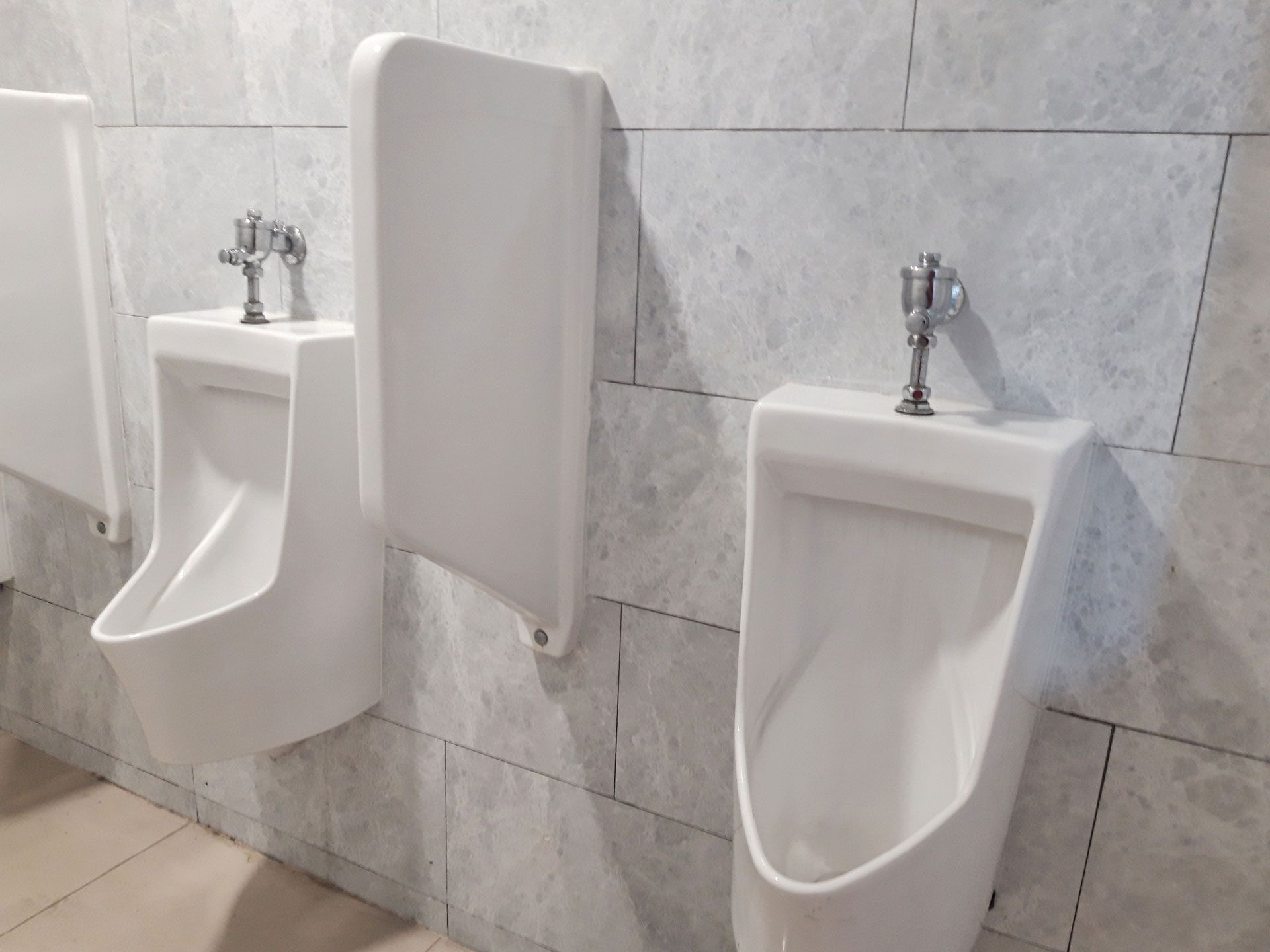 Two white urinals in a tiled restroom, separated by a privacy divider.