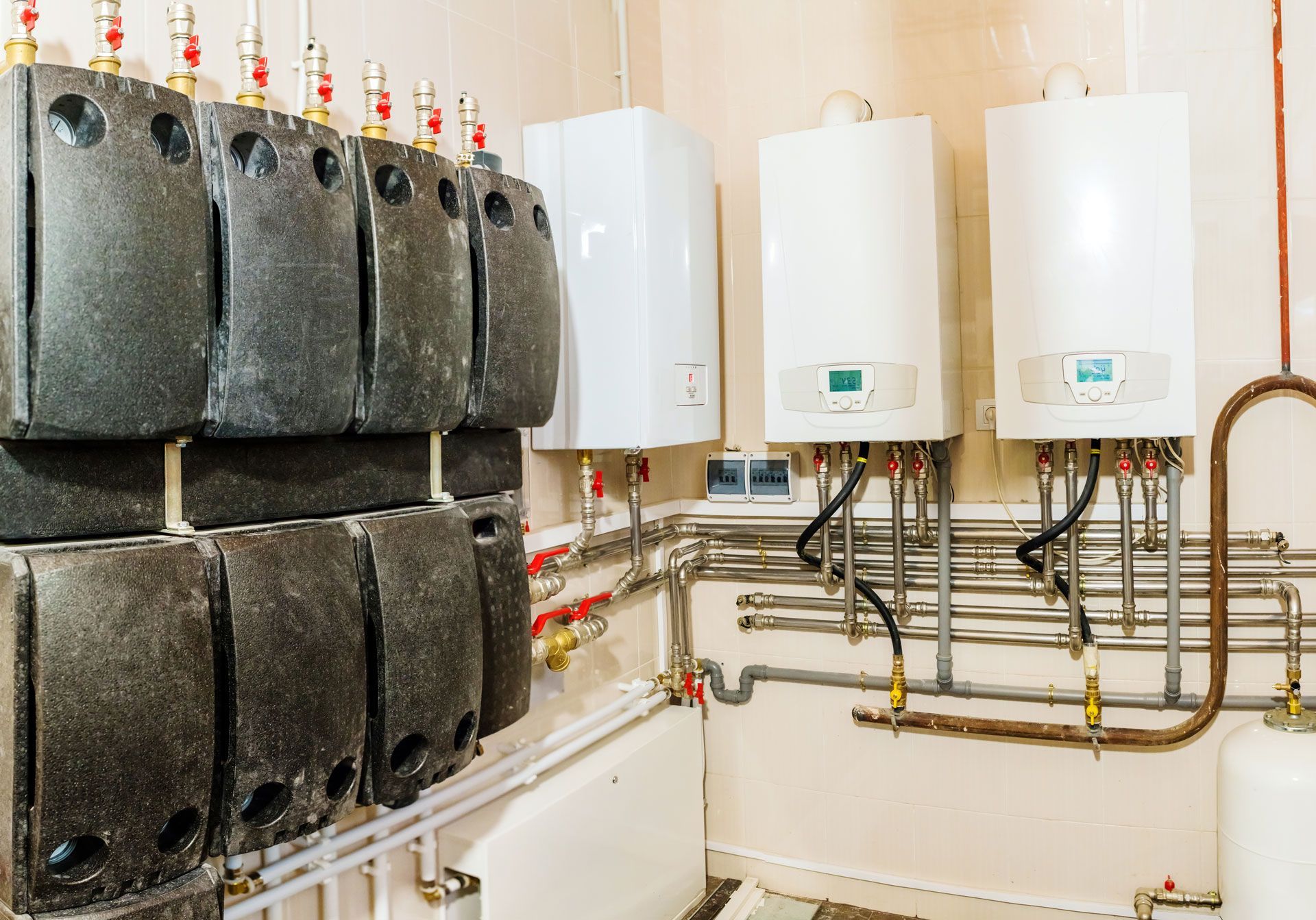 Wall-mounted water heaters and insulated storage tanks in a utility room with exposed plumbing
