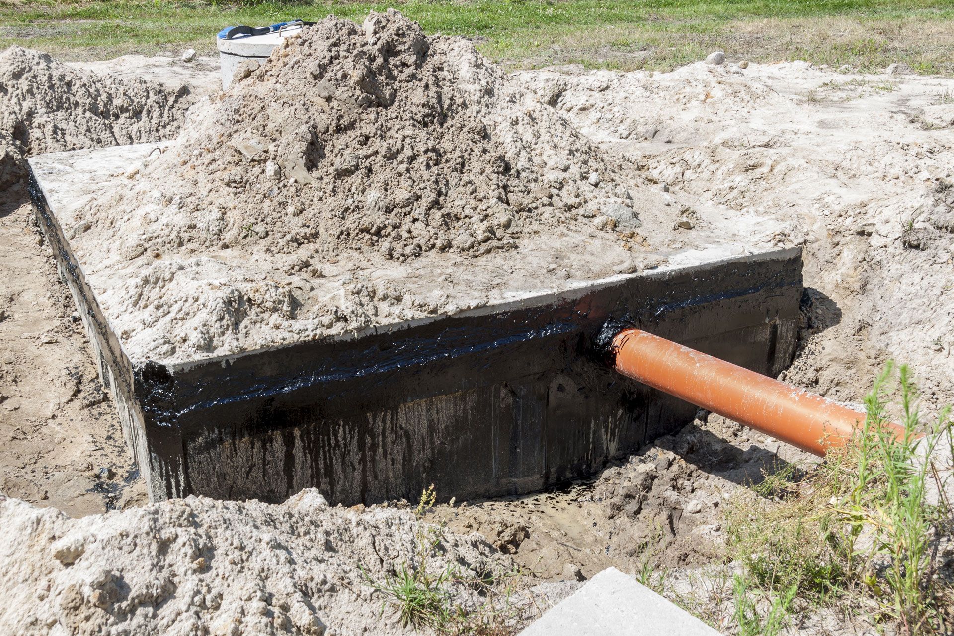 Black utility box in a sandy trench with an orange pipe extending from the side.