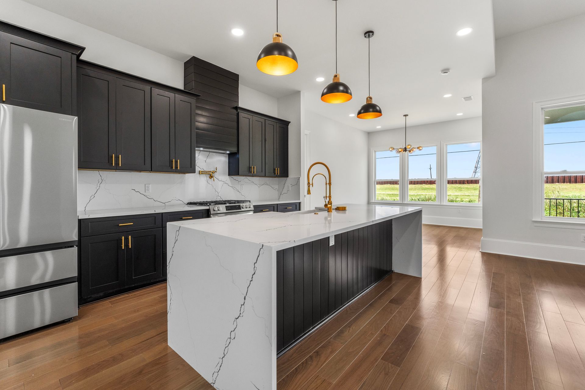A kitchen with black cabinets , white counter tops , stainless steel appliances and a large island.