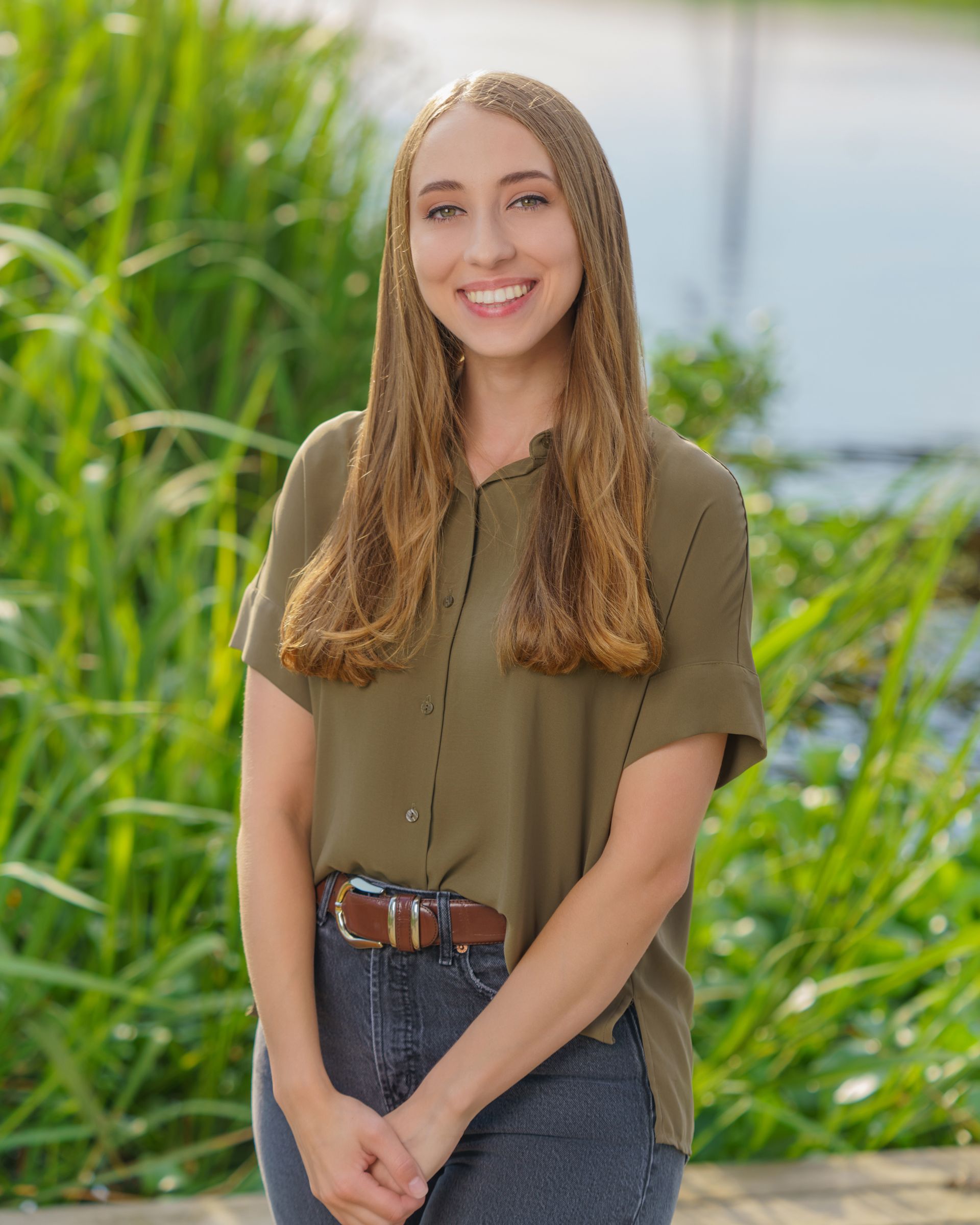 A woman in a green shirt and blue jeans is standing in front of tall grass.