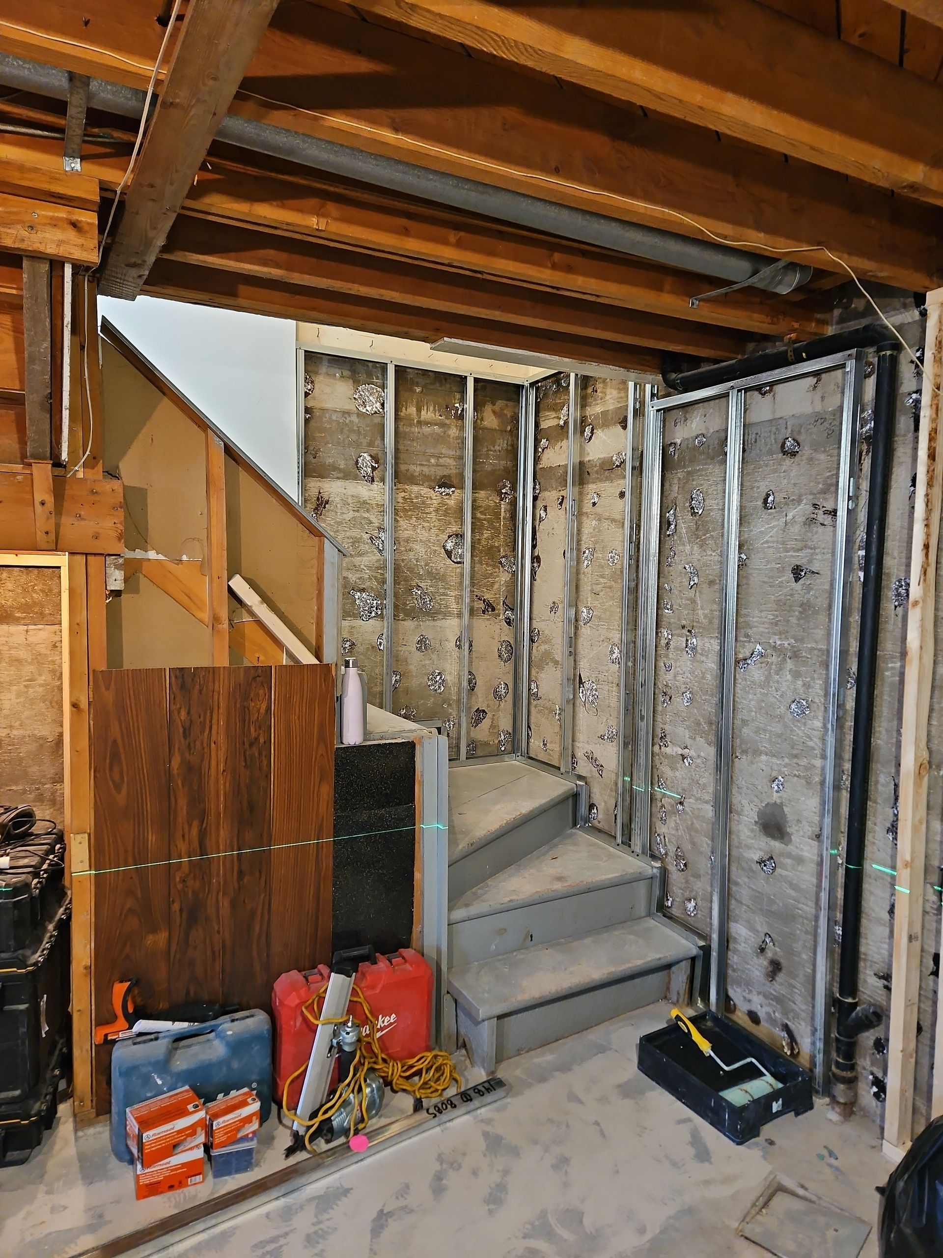 Sous-sol en construction : ossature métallique apparente, isolation et escalier. Outils et fournitures sont à disposition.