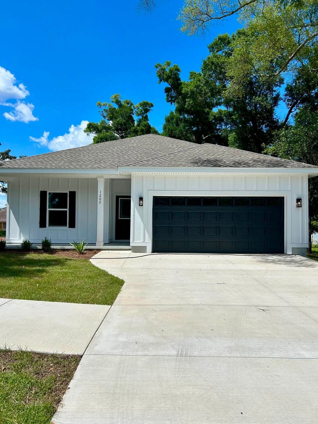 Single-story white house with black garage door and driveway under a bright blue sky
