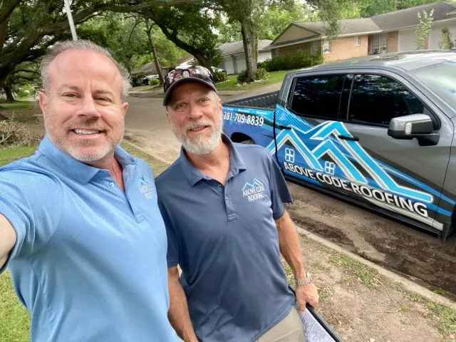 Two men smiling in front of a blue and grey truck with