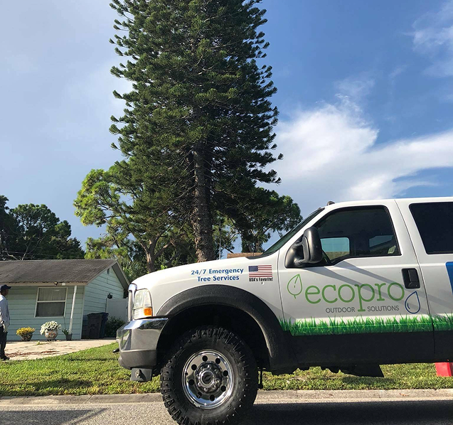 White EcoPro truck parked on the street in front of a house with a tall tree and a blue sky.