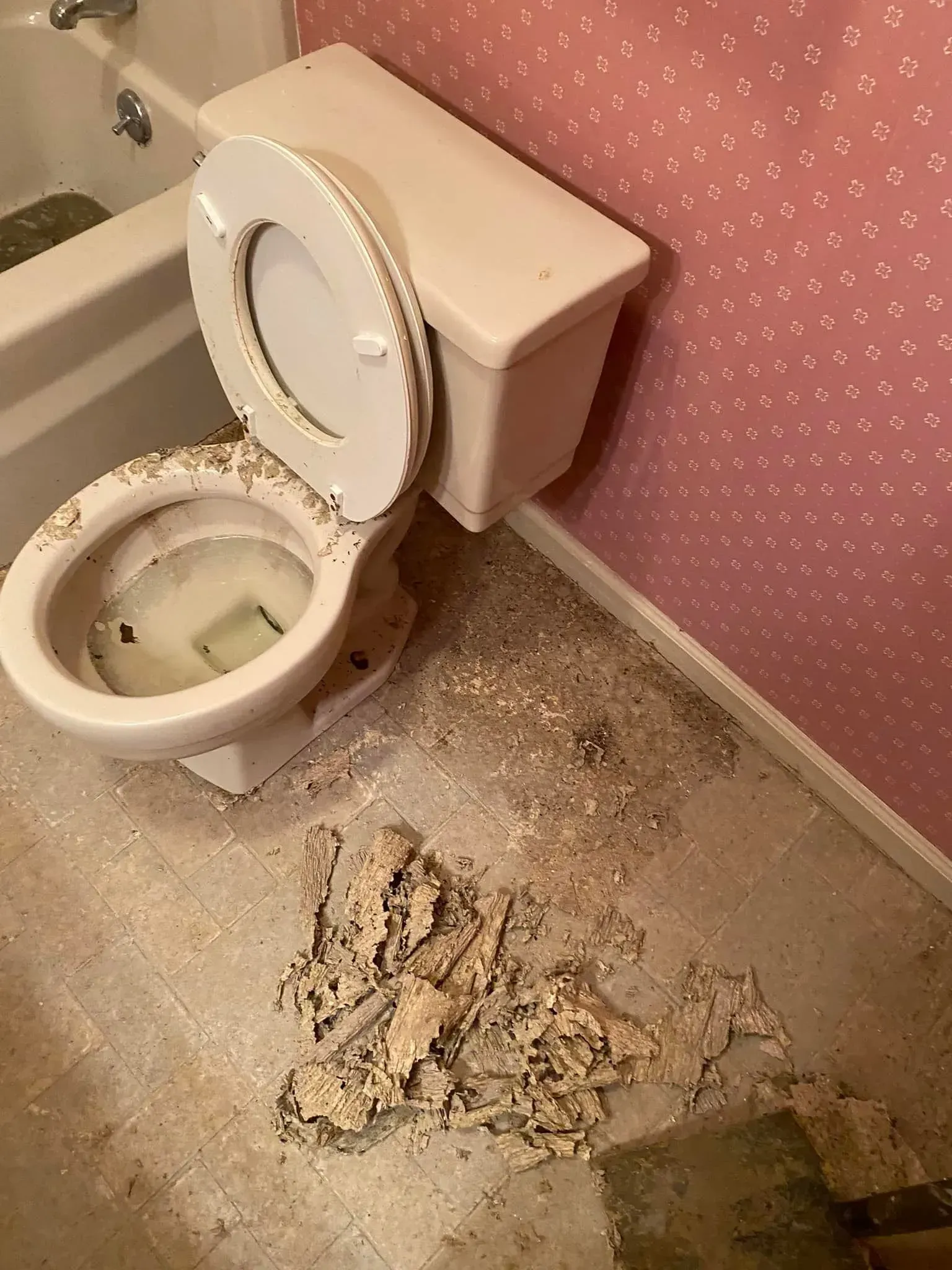 Damaged bathroom with open toilet and debris scattered on the floor near the wall